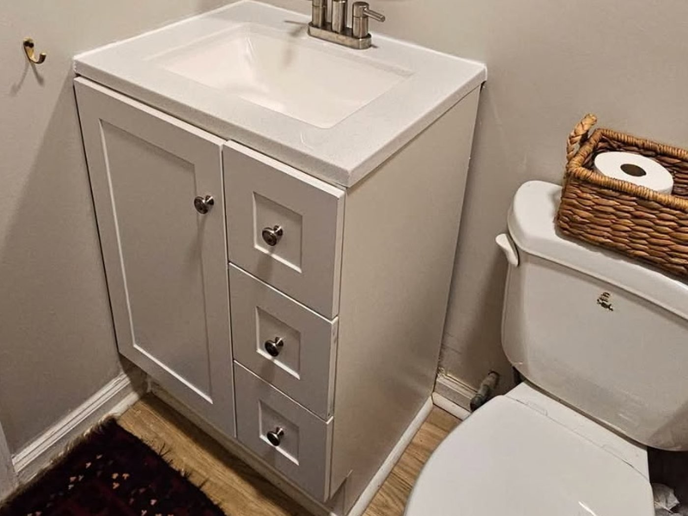 Bathroom vanity and faucet installation: the half bath after, with a clean white vanity, new faucet and a fresh rug.