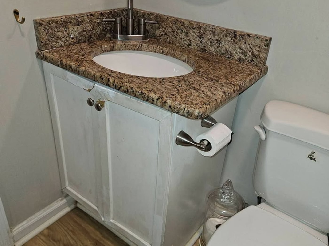 Before the vanity replacement: the same half bath with a chipped cabinet and a speckled granite top.